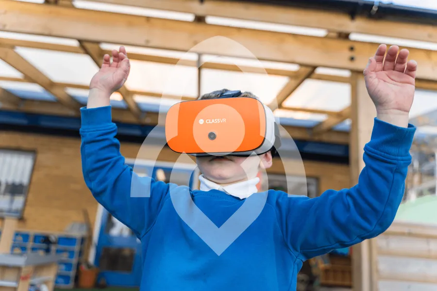 A primary school pupil wearing a ClassVR headset outdoors, hands raised as they explore a virtual environment.