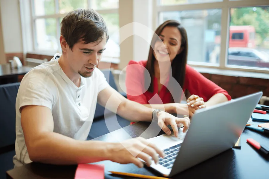 Two young colleagues sitting side by side at a laptop, working through a task together.